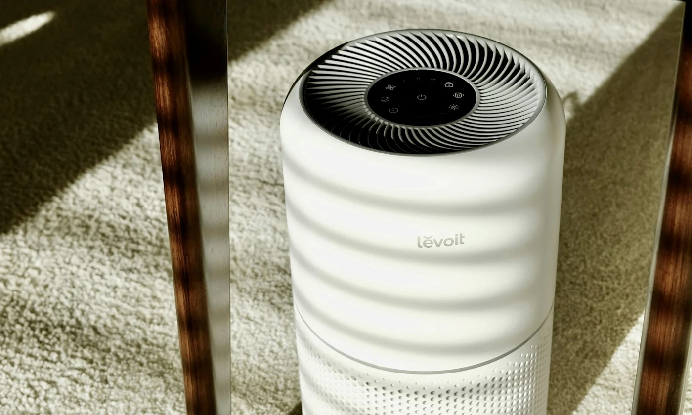 White Levoit air purifier on a sunlit carpet beneath a wooden table