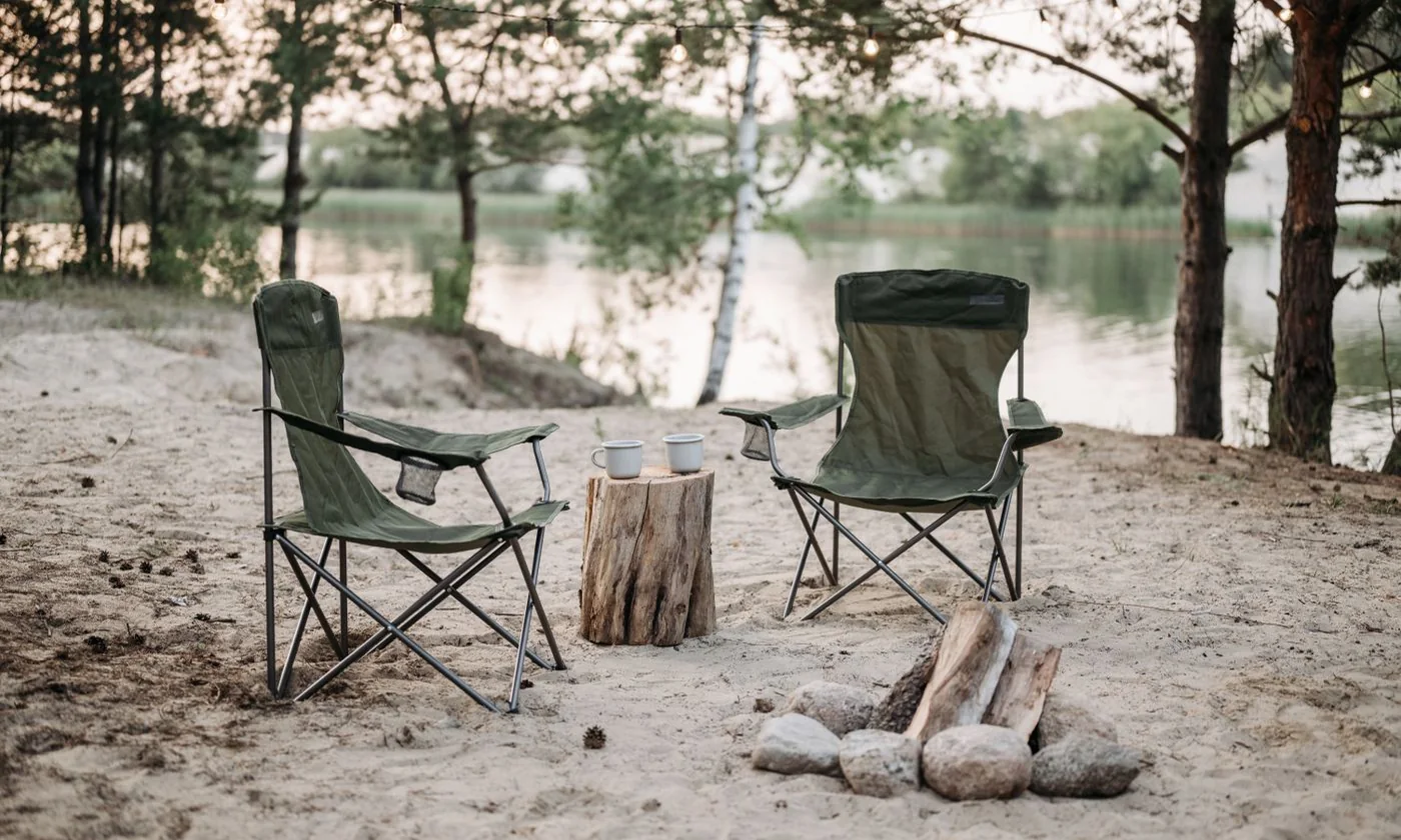 Folding camping chairs beside a lake and a wooded shoreline