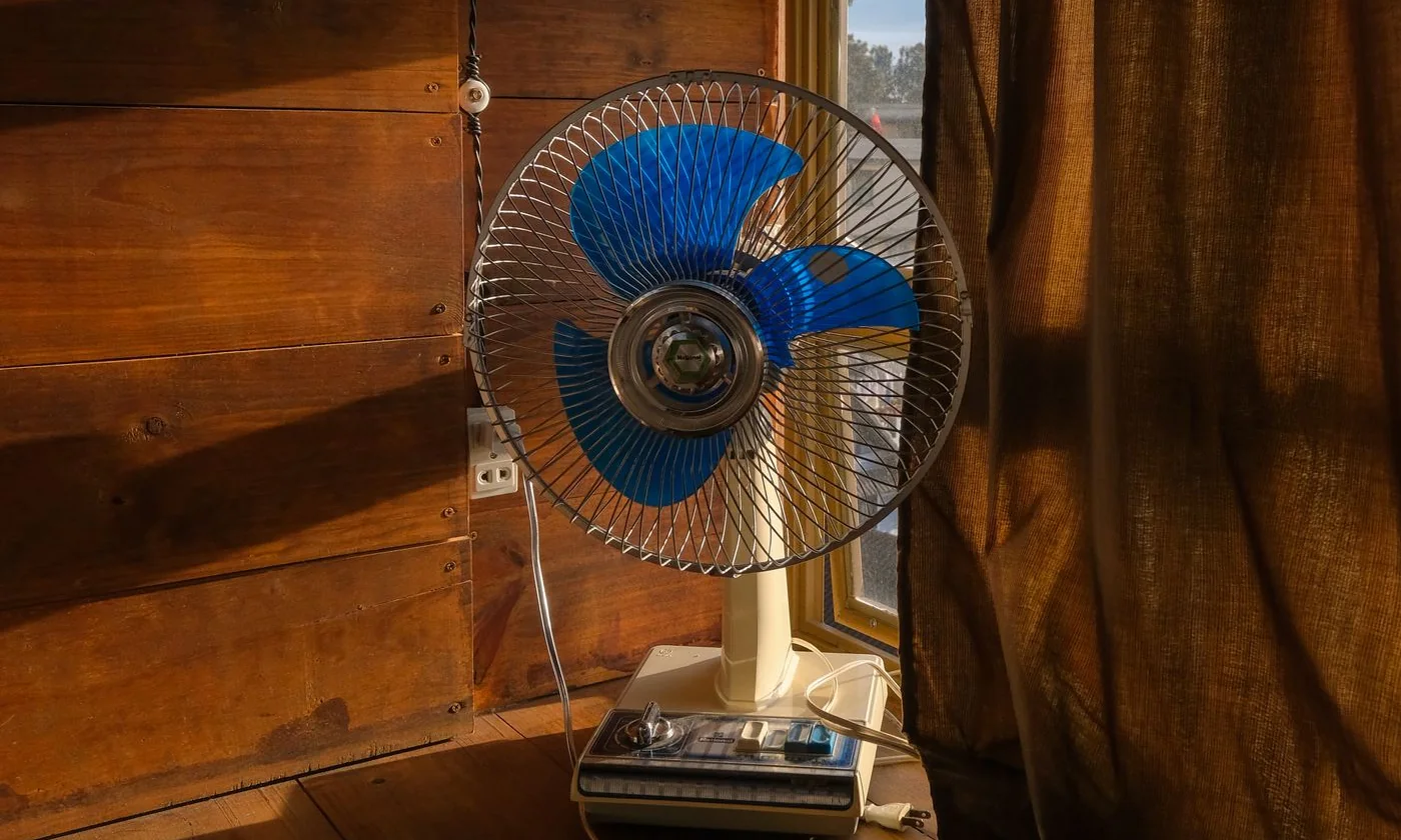 Electric fan beside a window with sunlight on the wooden wall