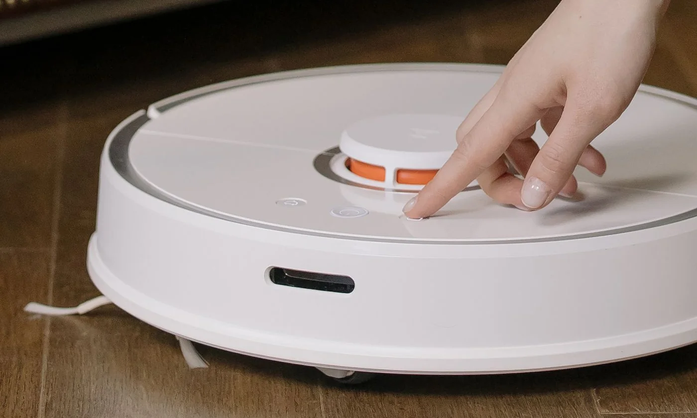 A hand starting a robot vacuum on a wooden floor