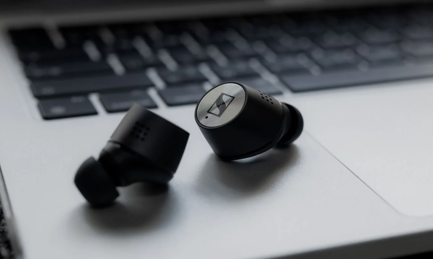 Black wireless earbuds resting on a silver laptop keyboard